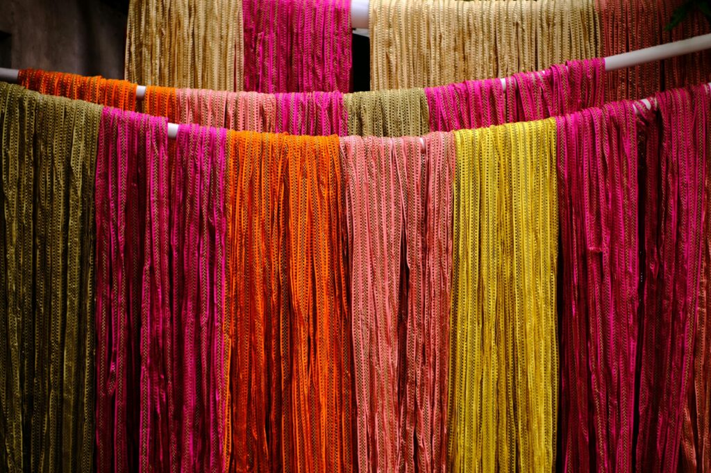 Vibrant vertical rows of hand-dyed pink, orange, and gold textiles hanging in a traditional workshop, representing cultural heritage and design precision.