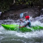 ​A whitewater kayaker in a red helmet paddling dynamically through powerful river rapids, representing action from the Malabar River Festival 2026.