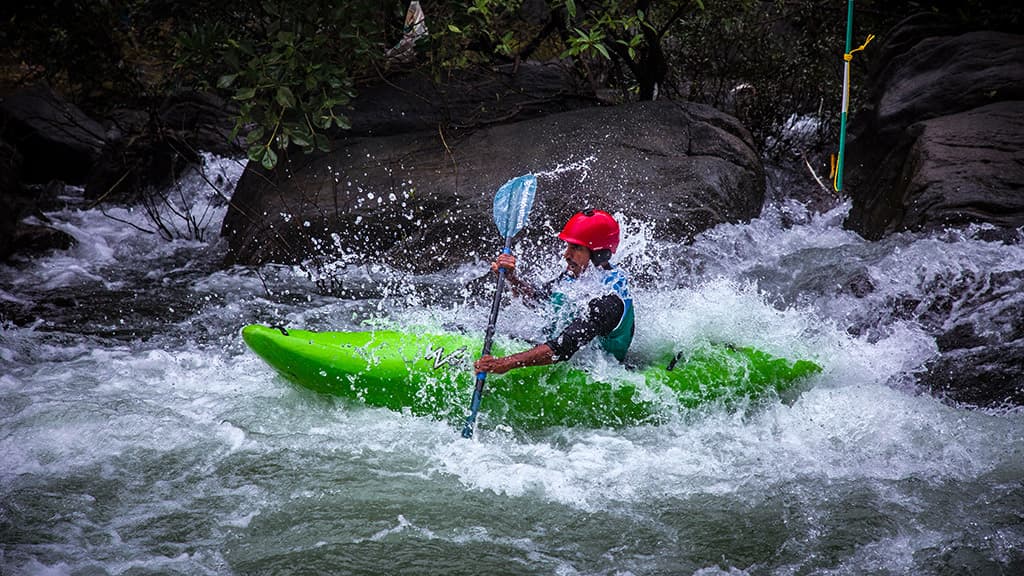 ​A whitewater kayaker in a red helmet paddling dynamically through powerful river rapids, representing action from the Malabar River Festival 2026.